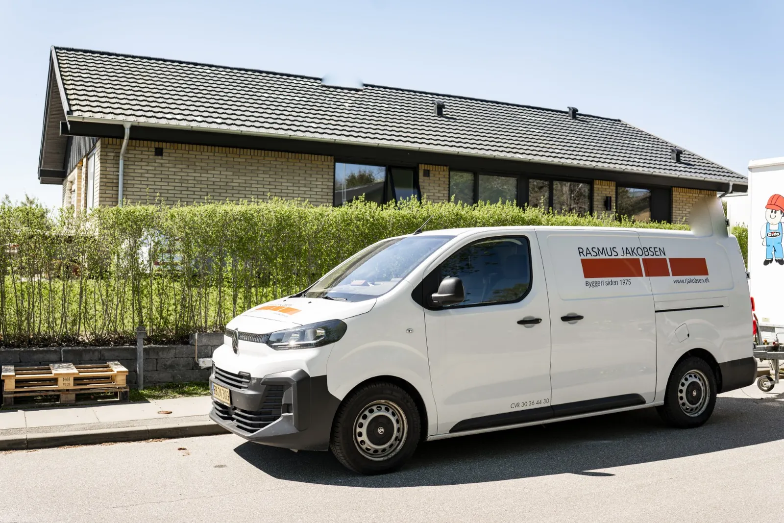 Hvid R. Jakobsen-håndværkerbil parkeret foran et gult murstenshus i villakvarter