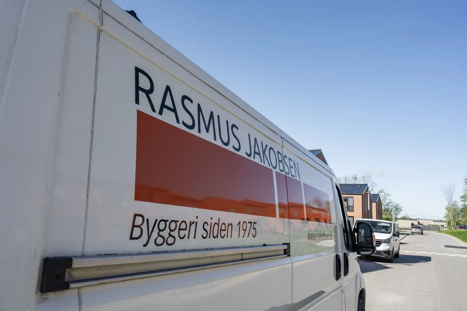 Hvid R. Jakobsen-varevogn på vej foran nybyggede rækkehuse i røde mursten